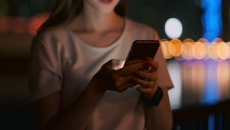 Close-up-of-a-young-girl-holding-a-smartphone-in-Dubai-at-night-and-writing-a-text-message